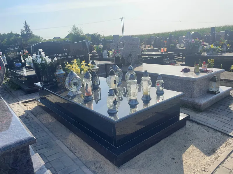 Grobowiec Impala z szeroką płaską płytą obsypaną lampionami, panorama cmentarza w tle, realizacja Kamileo Kraków.
